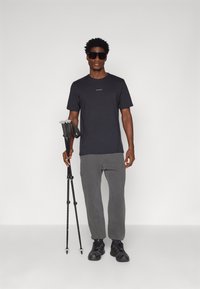 Black short-sleeve shirt with a small logo, gray fleece pants, and black hiking boots. Holding black trekking poles with gray accents.