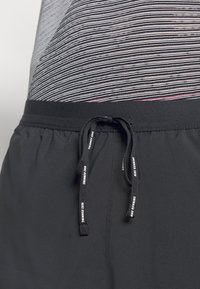Pantalones cortos deportivos negros con cordón y detalles reflectantes, cintura elástica, combinados con una camiseta a rayas en tonos gris y rosa.