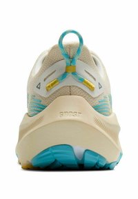 Béžová běžecká obuv z pohledu zezadu, se modrožlutým poutkem, texturovaným béžovým svrškem a modrou podešví, na patě je vyraženo "GHOST".