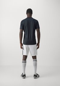 Svart trenings skjorte med korte ermer, hvite shorts med svarte detaljer, grå sokker med svarte striper og svarte treningssko, sett bakfra.