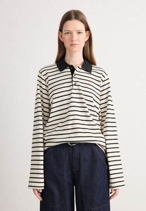 Black and white striped long-sleeve polo shirt with a black collar, featuring a small red logo and a relaxed fit, paired with dark denim pants.