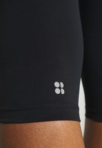 Černé kompresní šortky vyrobené z hladké tkaniny. Mají malé šedé logo na boku a zesílený šev podél lemu.