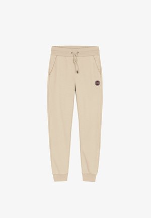 Bežové tepláky s elastickým pásom, šnúrkou, dvoma bočnými vreckami a okrúhlym logom na ľavom stehne. S manžetami na členkoch.