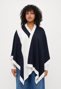 Navy a bílý barevně blokovaný pončo s výstřihem do V, s texturovaným povrchem a kontrastním lemem podél okrajů.