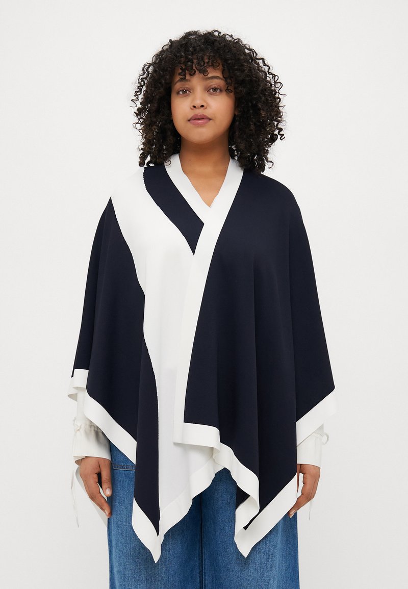 Navy a bílý barevně blokovaný pončo s výstřihem do V, s texturovaným povrchem a kontrastním lemem podél okrajů.