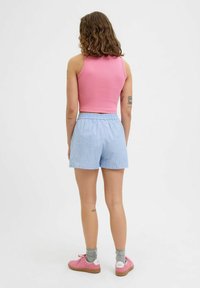 Roza rebrasta majica brez rokavov, kombinirana z svetlo modrimi kratkimi hlačami s črtami. Obleka ima elastičen pas in rožnate teniske z sivimi nogavicami.