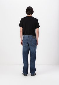 Camiseta negra de manga corta y vaqueros de pierna ancha de color azul oscuro. Los vaqueros cuentan con un diseño de bolsillo trasero y una etiqueta de marca visible cerca de la cintura.