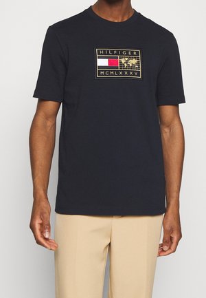 Granatowy bawełniany t-shirt z krótkimi rękawami, z prostokątnym haftowanym logo w kolorach złotym, czerwonym i białym. Miękka tekstura, klasyczny fason z okrągłym dekoltem.