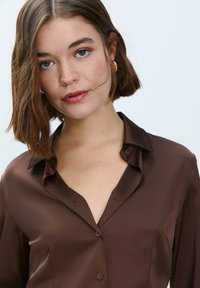 Brown satin shirt with a collared neckline, subtle sheen, button front, and a relaxed fit, showcasing minimalistic design.