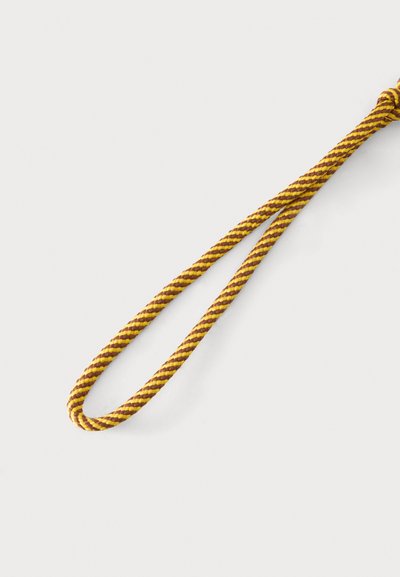 Corde torsadée jaune et marron formant une boucle sur un fond clair uni.