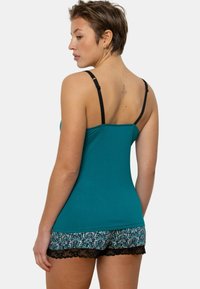 Débardeur bleu sarcelle avec bretelles noires, associé à un short à motifs floraux avec une bordure en dentelle à l'ourlet.