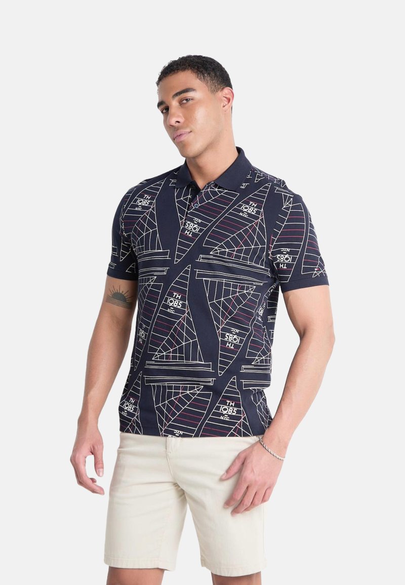Polo de navy con patrones geométricos de veleros blancos y acentos de texto. Manga corta y cuello clásico, fabricado en una tela transpirable.