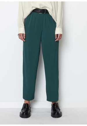 Tealfarbene, locker sitzende Hose mit einem elastischen Bund, kombiniert mit einem schwarzen Gürtel. Akzentuiert durch klobige schwarze Schuhe und strukturierten Stoff.