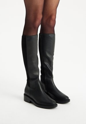 Czarne skórzane kozaki za kolano o eleganckim designie, z bocznym zamkiem błyskawicznym, okrągłym noskiem i minimalnym obcasem blokowym dla stabilności.