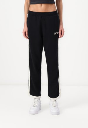 Svarte joggebukser med hvite sidestropper, elastisk midje, og Roxy-logo på hoften. Kombinert med hvite joggesko. Glatt tekstur.