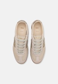 Beige leather sneakers with a textured snake print accent, flat laces, and gold logo detailing on the tongue and side.