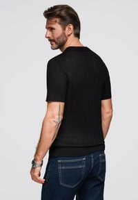 Black short-sleeve knitted top with a ribbed texture, paired with dark blue jeans. View shows the back and the design details of the shirt.
