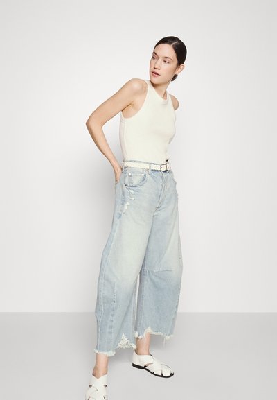 Top bianco, jeans larghi strappati blu chiaro, e sandali bianchi con fasce incrociate. Design semplice con una vestibilità comoda.