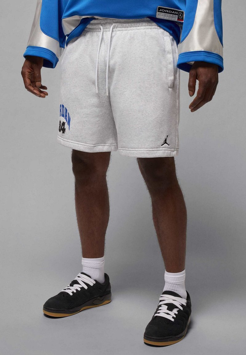 Pantalones cortos de algodón gris con la inscripción "JORDAN 84" en azul y negro, combinados con zapatillas negras y calcetines blancos. Corte holgado, cintura elástica.