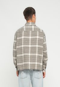 Flanellipaita beige ja harmaassa ruudullisessa kuosissa, napitettu kaulus, rento malli ja pitkät hihat, yhdistettynä vaaleansinisiin farkkuihin.