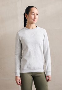 Lys grå sweatshirt med ribbestrikket hals og mansjetter, med subtil merkevare på forsiden og tekst langs ermet; brukt med olivengrønne tights.