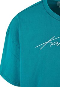 Zila kokvilnas T-krekls ar īsām piedurknēm, ar baltu izšūtu logo uz priekšu un klasisku apaļo kakla izgriezumu. Gluda tekstūra.