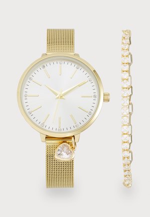 Guldfarvet mesh rem ur med hvid urskive, kvartsbevælgelse og krystalaccenter. Leveres med et matchende guldbelagt armbånd med klare sten.