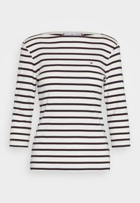 Randig tröja med lång ärm i vitt och marinblått med horisontella ränder, utrustad med båtkrage och en liten logga på bröstet. Tillverkad i bomull.