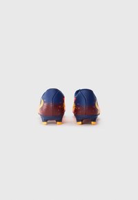 Une paire de chaussures de football bleu foncé et orange vue de l'arrière sur un fond blanc uni.