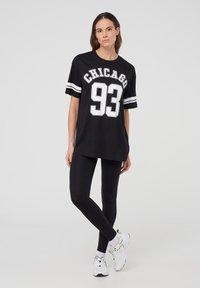T-shirt nera oversize a maniche corte con la scritta "CHICAGO 93" stampata in bianco, abbinata a leggings neri e sneakers bianche con dettagli.