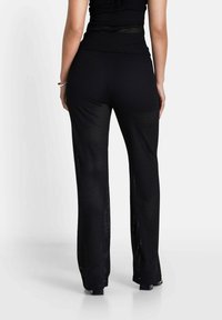 Zwarte gebreide broek met een losse pasvorm, voorzien van een gestructureerd, semi-doorschijnend ontwerp en uitlopende pijpen, die boven de enkel eindigen.