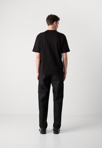 Black cotton t-shirt with a crew neck, paired with dark denim trousers. The outfit features a relaxed fit and minimalistic design.