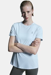 Ljust blå kortärmad träningsshirt gjord av ett slätt, andningsbart material. Har en rundad halsringning och en diskret logotyp på bröstet.