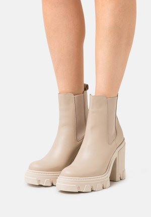 Beige Leder Stiefeletten mit elastischen seitlichen Einsätzen, klobigen strukturierten Sohlen und hohen Blockabsätzen, die über eine glatte Oberfläche und eine abgerundete Zehenpartie verfügen.