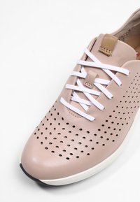 Baskets en cuir rose clair avec des lacets blancs, une tige perforée et une languette camel, vues de dessus sur un fond blanc.