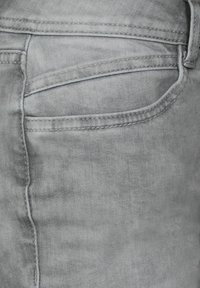 Vaaleanharmaat farkut, joissa on sileä pinta, takatasku ja kontrastiväriset saumat.