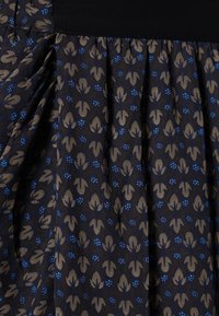 Tejido oscuro con un patrón floral repetido en beige y azul, que presenta pliegues y una textura suave. La cinturilla es de color negro sólido.