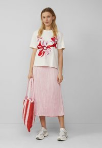 T-shirt blanc avec un motif floral rouge, associé à une jupe plissée rose. Les accessoires comprennent un sac fourre-tout rayé rouge et blanc et des baskets légères.