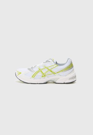 Chaussure de sport blanche avec une tige en mesh, des accents gris réfléchissants et des détails jaunes sur les panneaux latéraux et les lacets. Semelle en caoutchouc incluse.