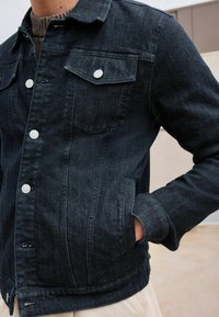 Dark denim jacket featuring a classic design, buttoned front, two chest pockets, and textured fabric with a slightly faded finish.