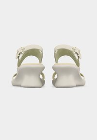 Μπεζ σανδάλια ανοιχτά μπροστά με ρυθμιζόμενα λουριά στον αστράγαλο και καλοσχηματισμένες, χαμηλές, χοντρές σόλες τακουνιών, εμφανιζόμενα από πίσω σε απλό φόντο.