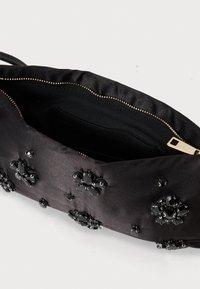 Fekete selyem clutch táska fekete gyöngyökkel díszített virágmintázattal és részben nyitott arany cipzárral, fehér háttérrel.
