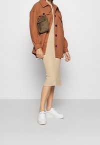 Rustrød, oversized uldjakke med sorte knapper, lagdelt over en tætsiddende, ribbet beige kjole. Hvide platform sneakers og en lille brun taske.