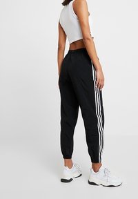 Svarta joggingbyxor med avsmalnande mudd, med tre vita ränder längs sidorna. Tillverkade av lätt material, kombinerat med vita sneakers.