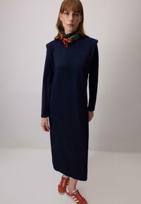 Tumesinine pika varrukaga kleit kõrge kaelusega ja õlavarre aktsentidega, kombinatsioonis punaste tossudega, millel on valged triibud.