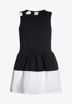 Ärmelloses Kleid mit einem schwarzen Baumwoll-Oberteil und einem weißen Lochspitzen-Unterteil. Es hat zwei kleine weiße Akzente an den Schultern und einen gerafften Taillenbereich.