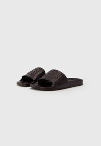 Black rubber slide sandals with wide straps featuring embossed branding. Open-toe design with a flat sole, smooth texture, and minimal detailing.
