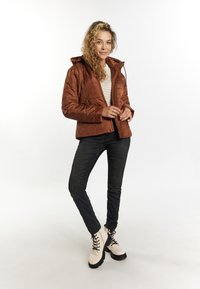 Brun quilted puffer-jakke med hætte, styling med sorte slim jeans og beige snøre støvler, med en stribet top under.
