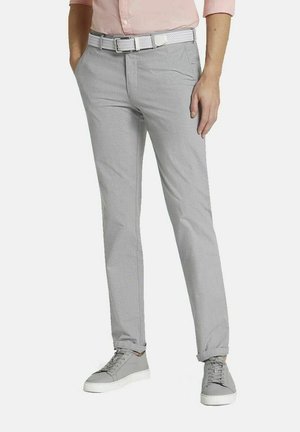 Homme portant un pantalon slim gris clair, une ceinture blanche tissée et des baskets grises assorties, debout les mains dans les poches.