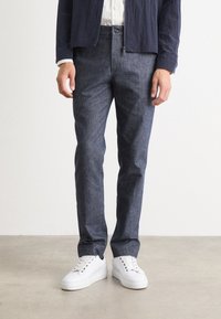 Ciemnoniebieskie dżinsy o slim fit z delikatną teksturą, w połączeniu z białymi trampkami o gładkiej powierzchni i sznurowaniu.